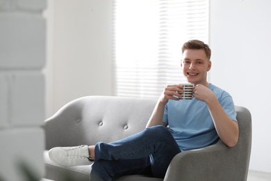 Photo of Teenage boy with cup sitting on sofa at home. Space for text