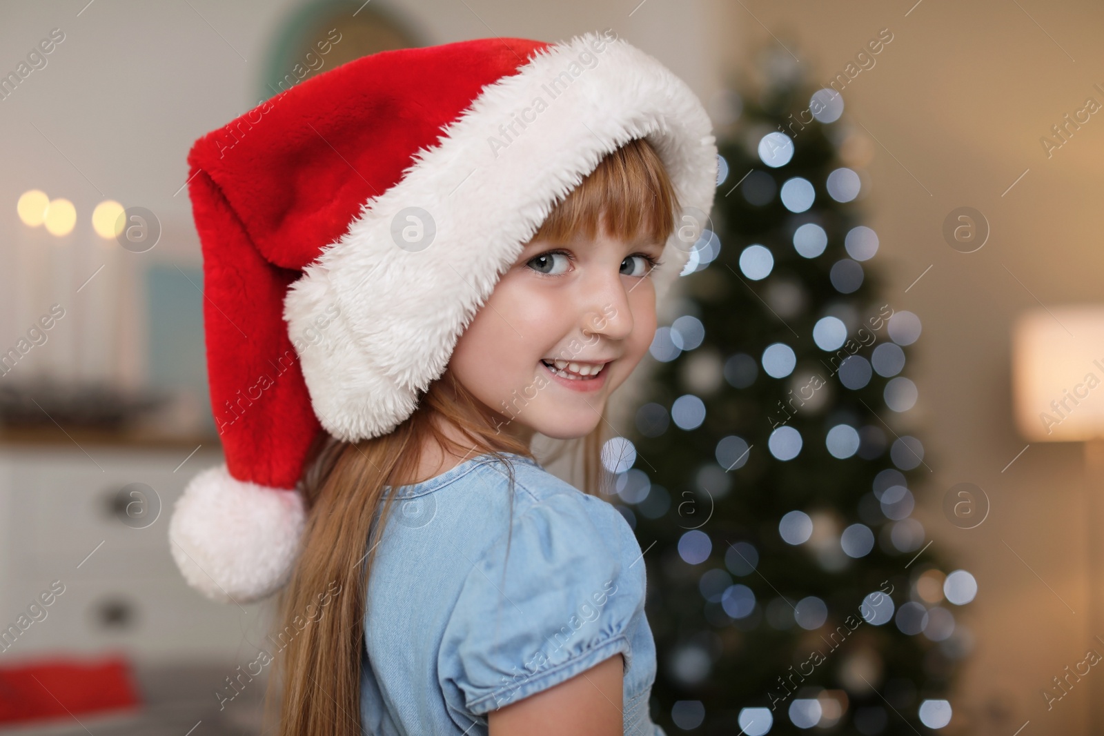 Photo of Cute little child in Santa hat at home. Christmas celebration