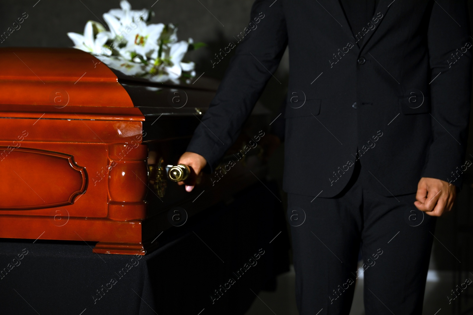 Photo of Young man carrying wooden casket in funeral home, closeup