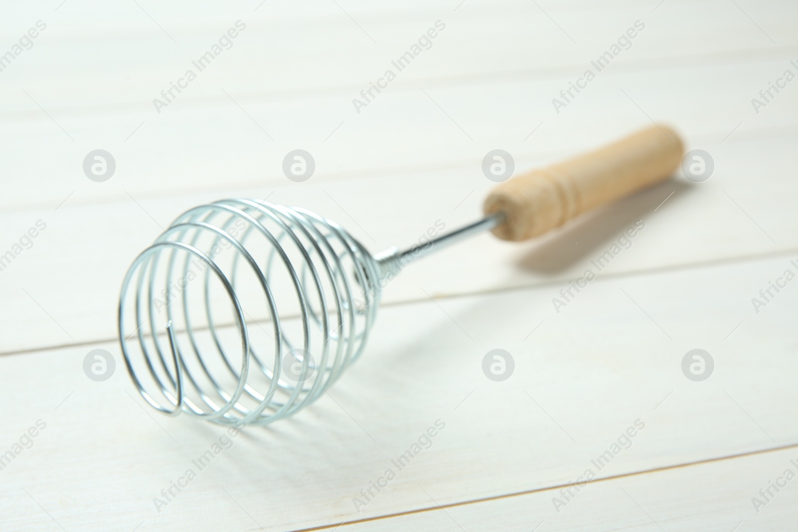 Photo of Metal spring whisk on white wooden table, closeup