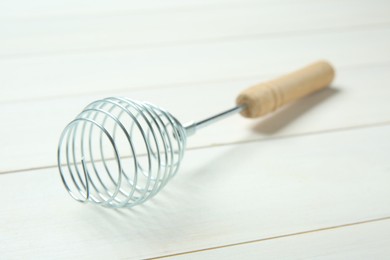 Photo of Metal spring whisk on white wooden table, closeup