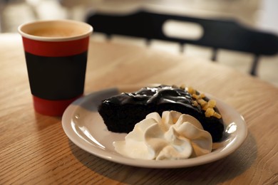 Photo of Tasty coffee in takeaway paper cup and dessert on wooden table at cafe, closeup