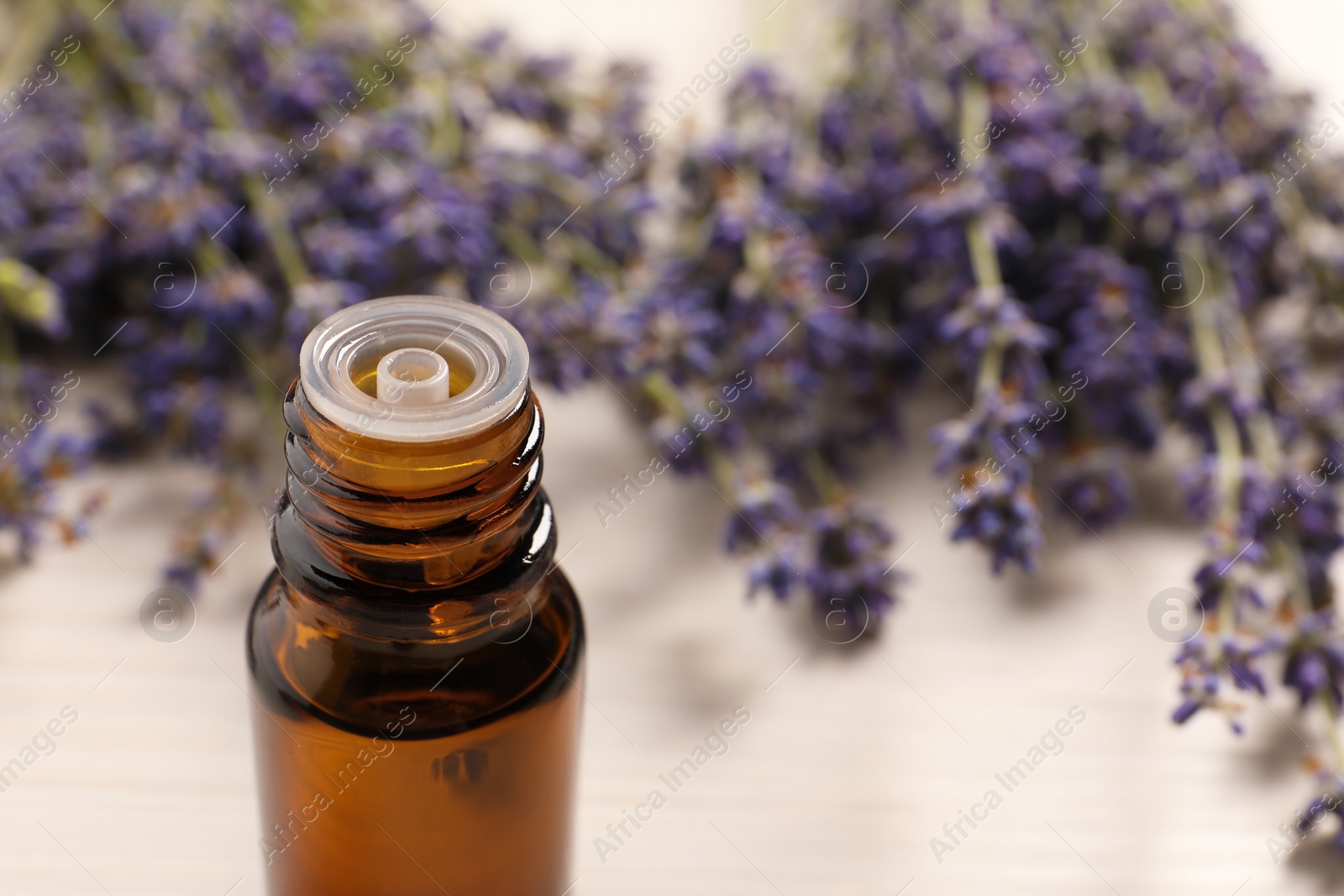 Photo of Bottle of essential oil and lavender flowers on white table, closeup. Space for text