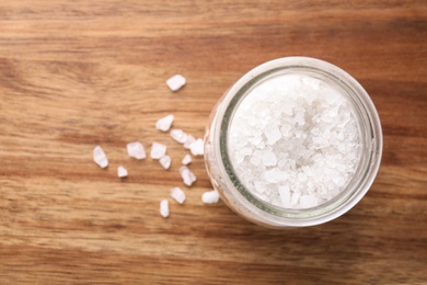 Photo of Jar of white sea salt on wooden table, top view with space for text. Spa treatment