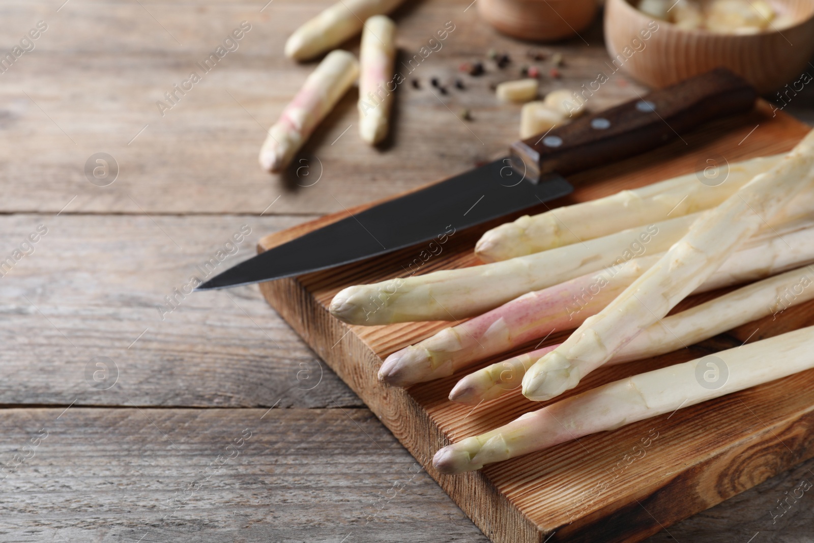 Photo of Fresh white asparagus, cutting board and knife on wooden table