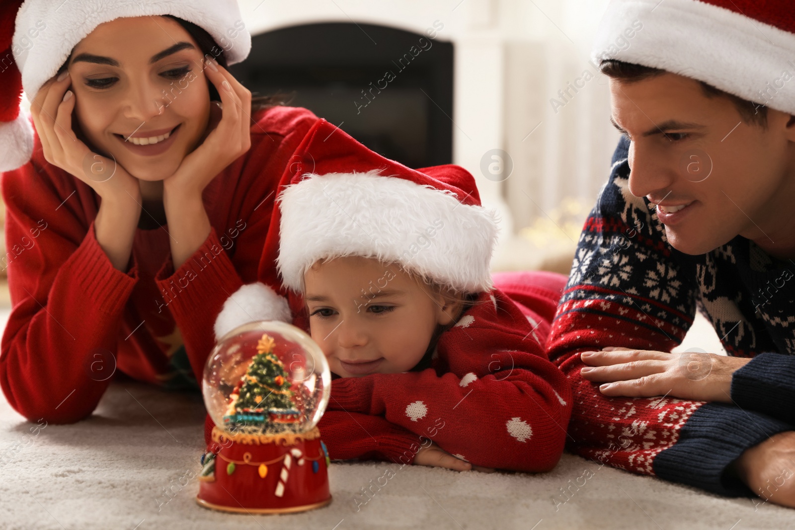 Photo of Family in Santa hats playing with snow globe while lying on floor