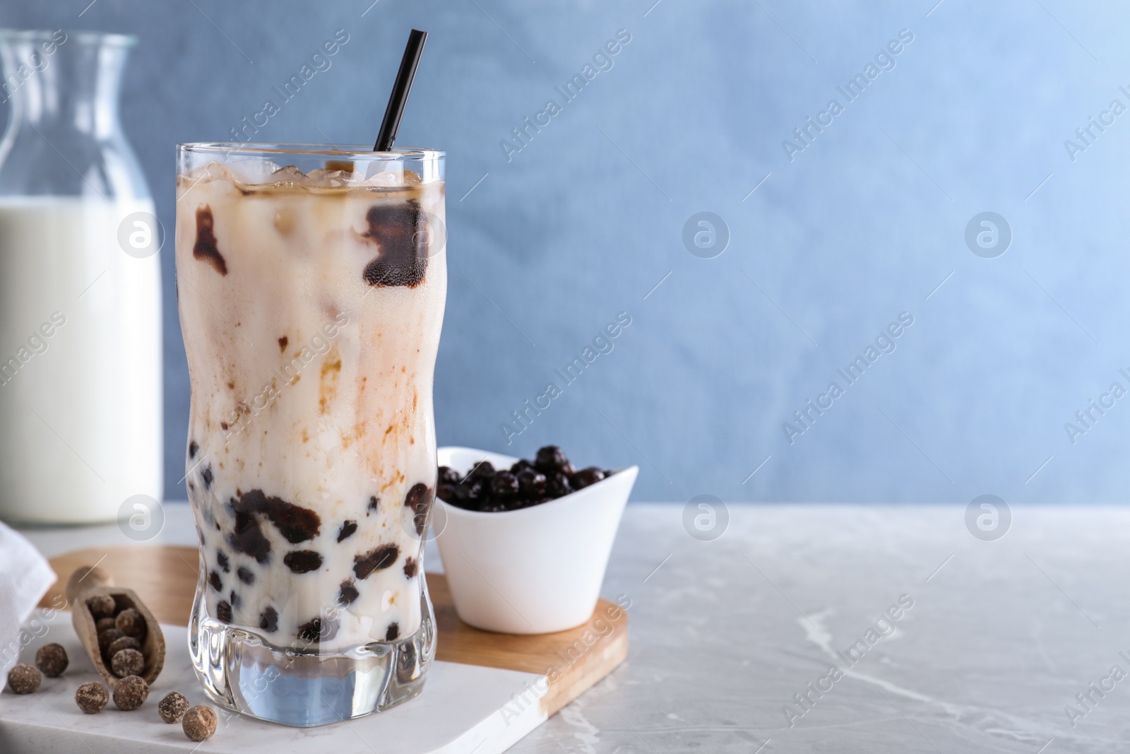 Photo of Bubble milk tea with tapioca balls on grey marble table against blue background. Space for text