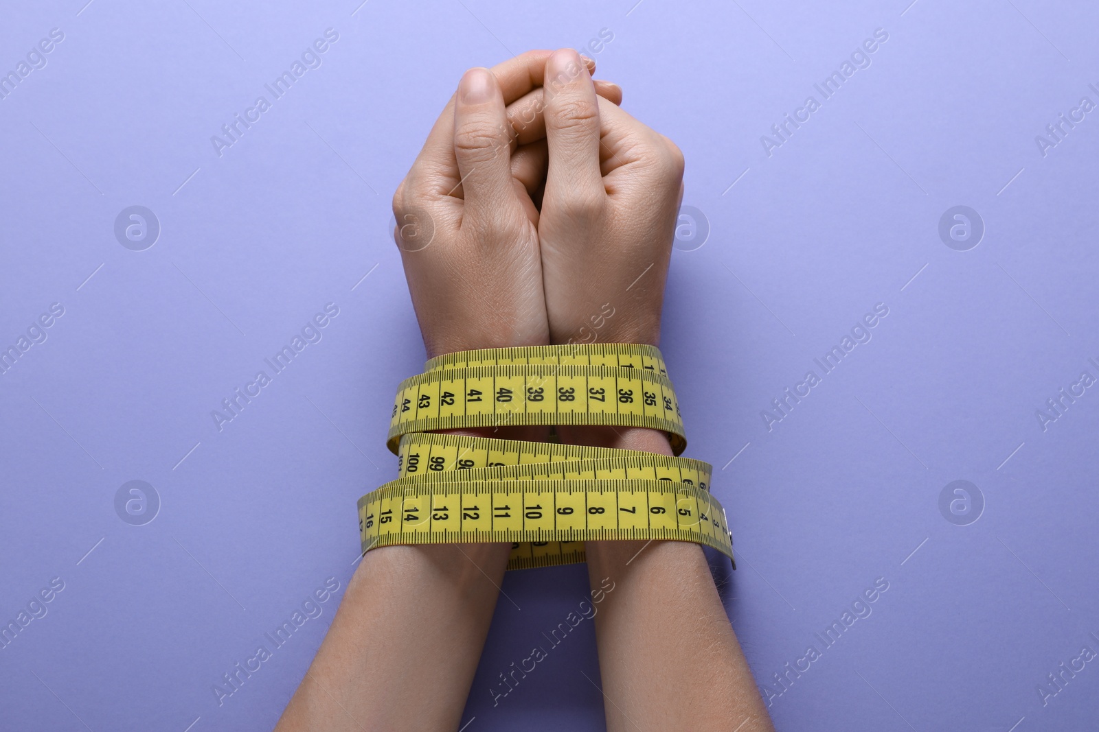 Photo of Woman tied with measuring tape on violet background, top view. Diet concept