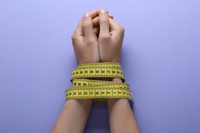 Woman tied with measuring tape on violet background, top view. Diet concept