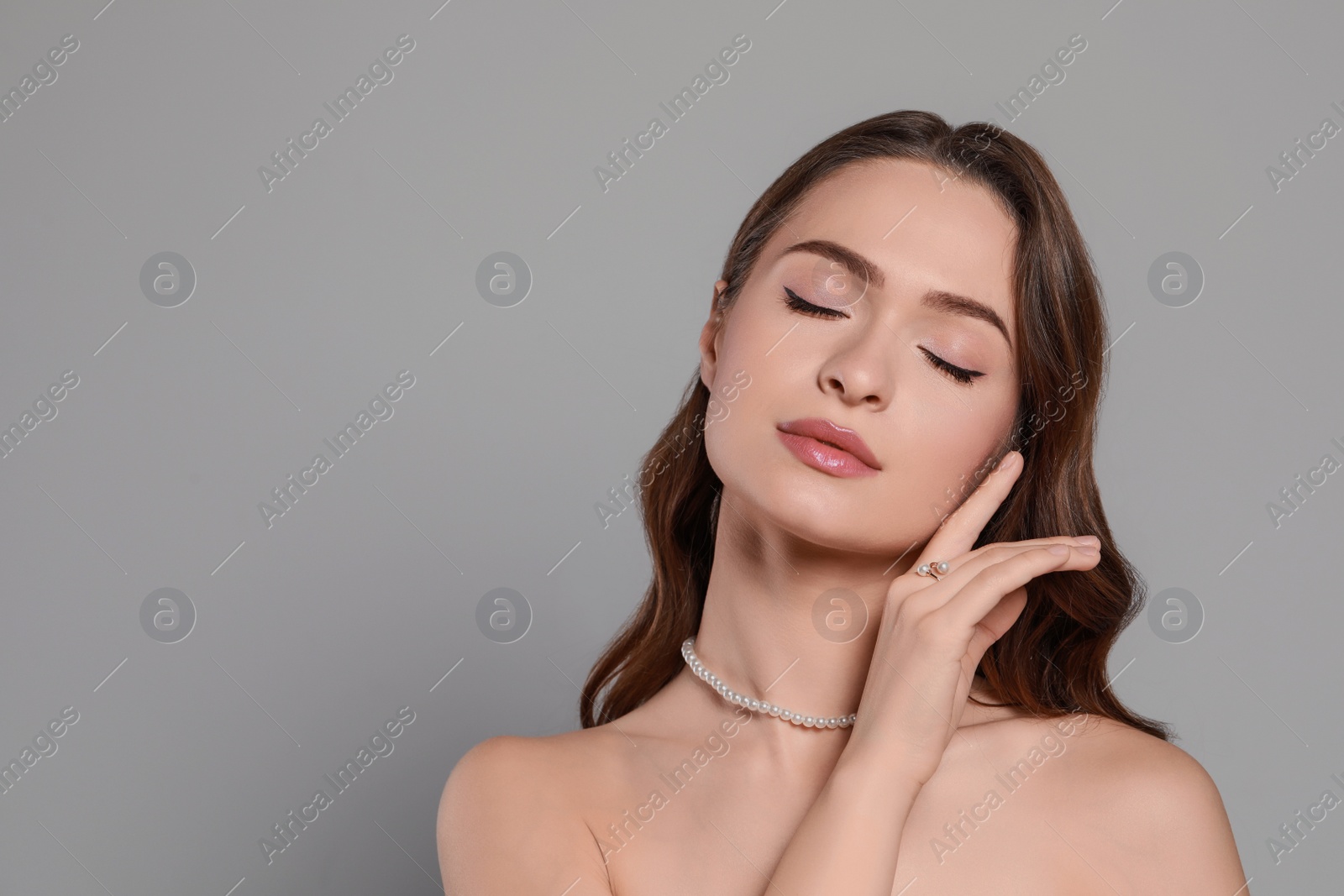 Photo of Young woman wearing elegant pearl jewelry on grey background, space for text