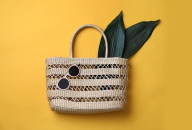 Photo of Stylish straw bag and sunglasses on yellow background, flat lay. Summer accessories