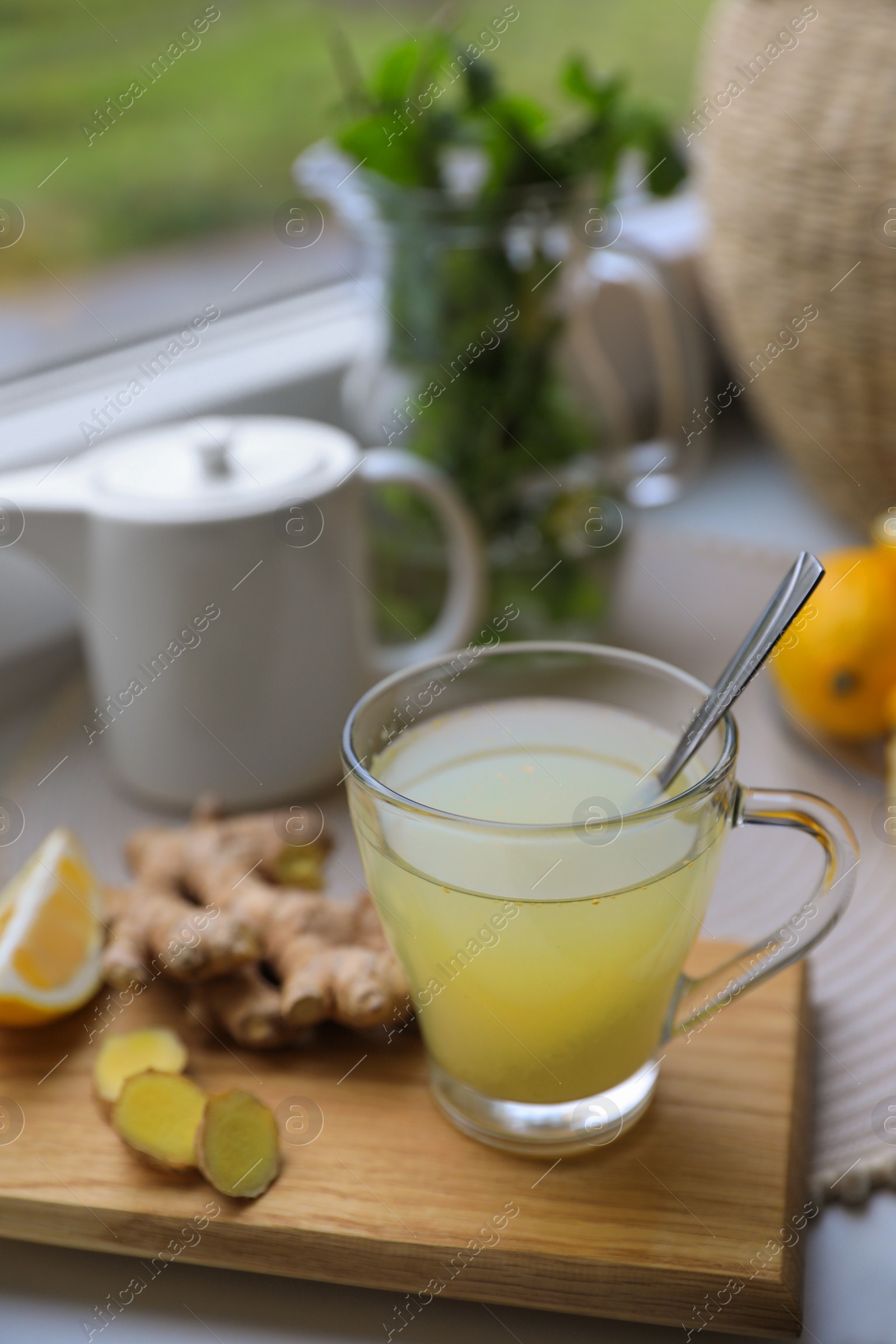 Photo of Glass of aromatic ginger tea and ingredients near window