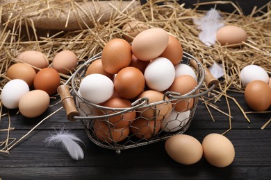 Fresh chicken eggs and dried straw on black wooden table