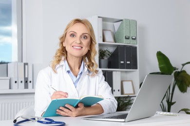 Photo of Doctor with laptop and notebook at desk in clinic. Online medicine concept