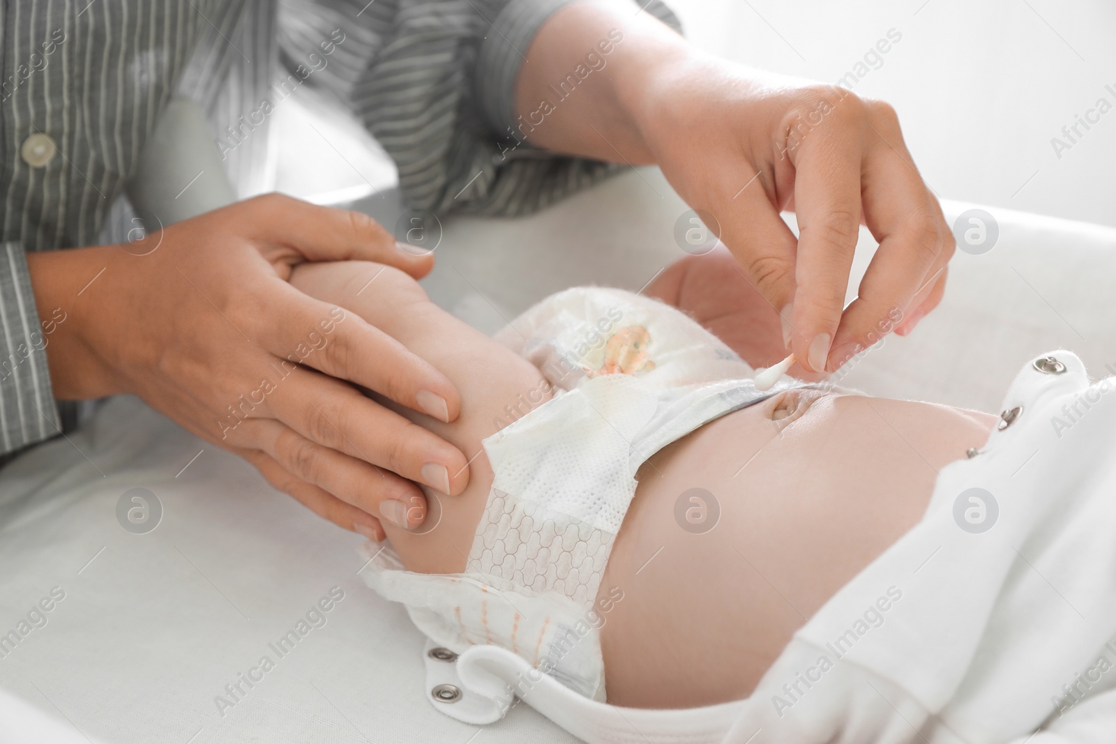 Photo of Mother cleaning navel of her baby with cotton bud on changing table, closeup