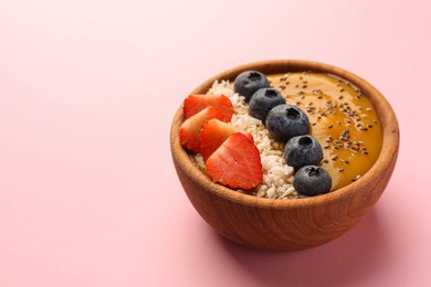 Photo of Delicious smoothie bowl with fresh berries, chia seeds and coconut flakes on pale pink background. Space for text