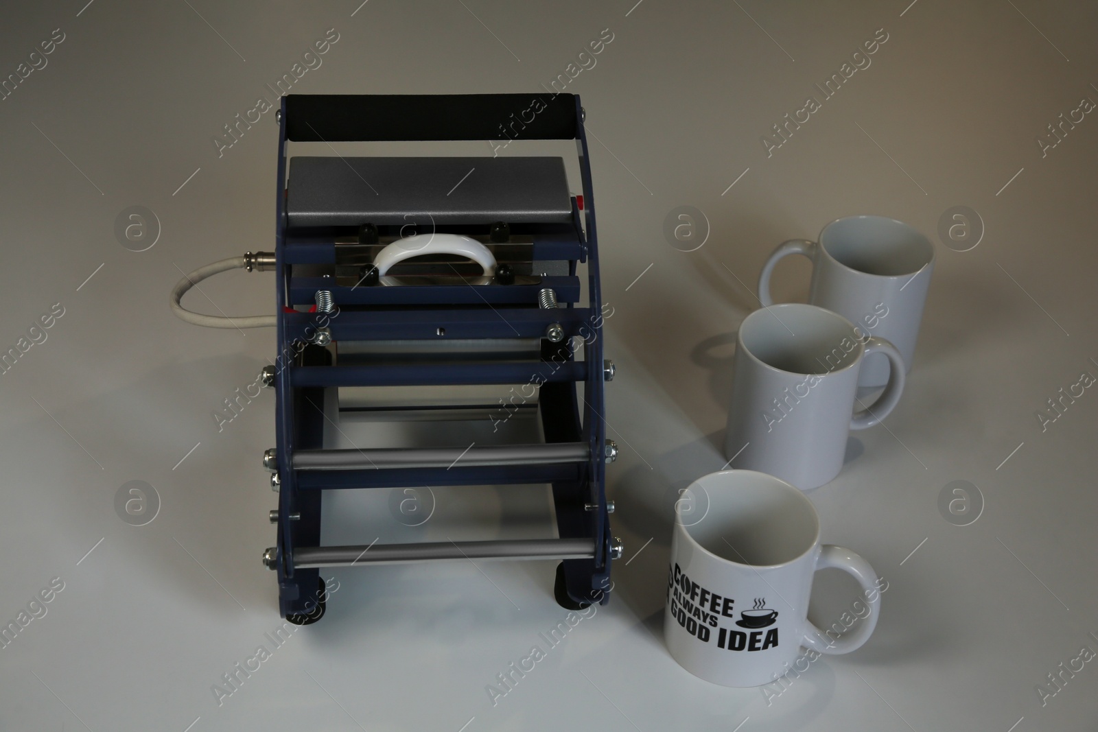 Photo of Printing logo. Heat press with cups on white table