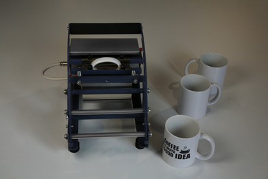 Photo of Printing logo. Heat press with cups on white table
