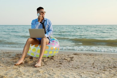 Photo of Happy businessman with laptop talking by mobile phone on beach. Business trip