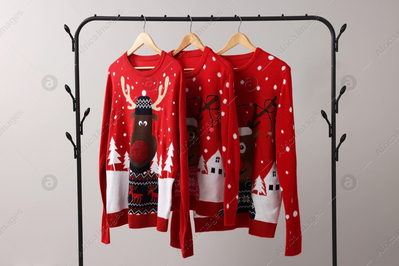 Photo of Different Christmas sweaters hanging on rack against light background