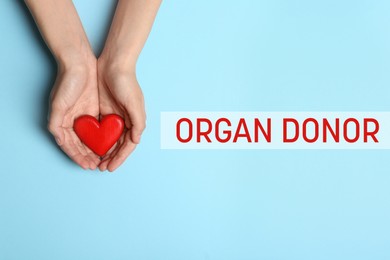 Organ donor. Woman holding heart on light blue background, top view