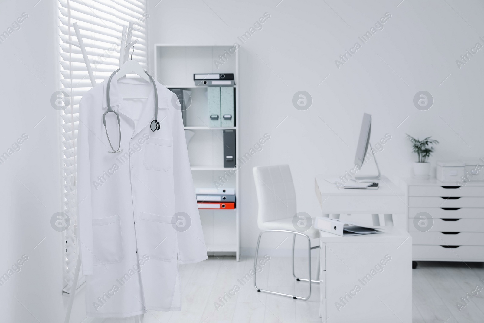 Photo of White doctor's gown and stethoscope hanging on rack in clinic