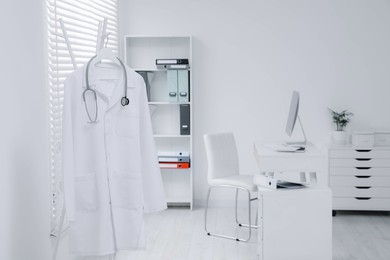 White doctor's gown and stethoscope hanging on rack in clinic