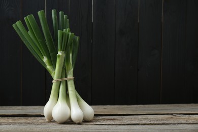 Photo of Bunch of fresh green spring onions on wooden table, space for text