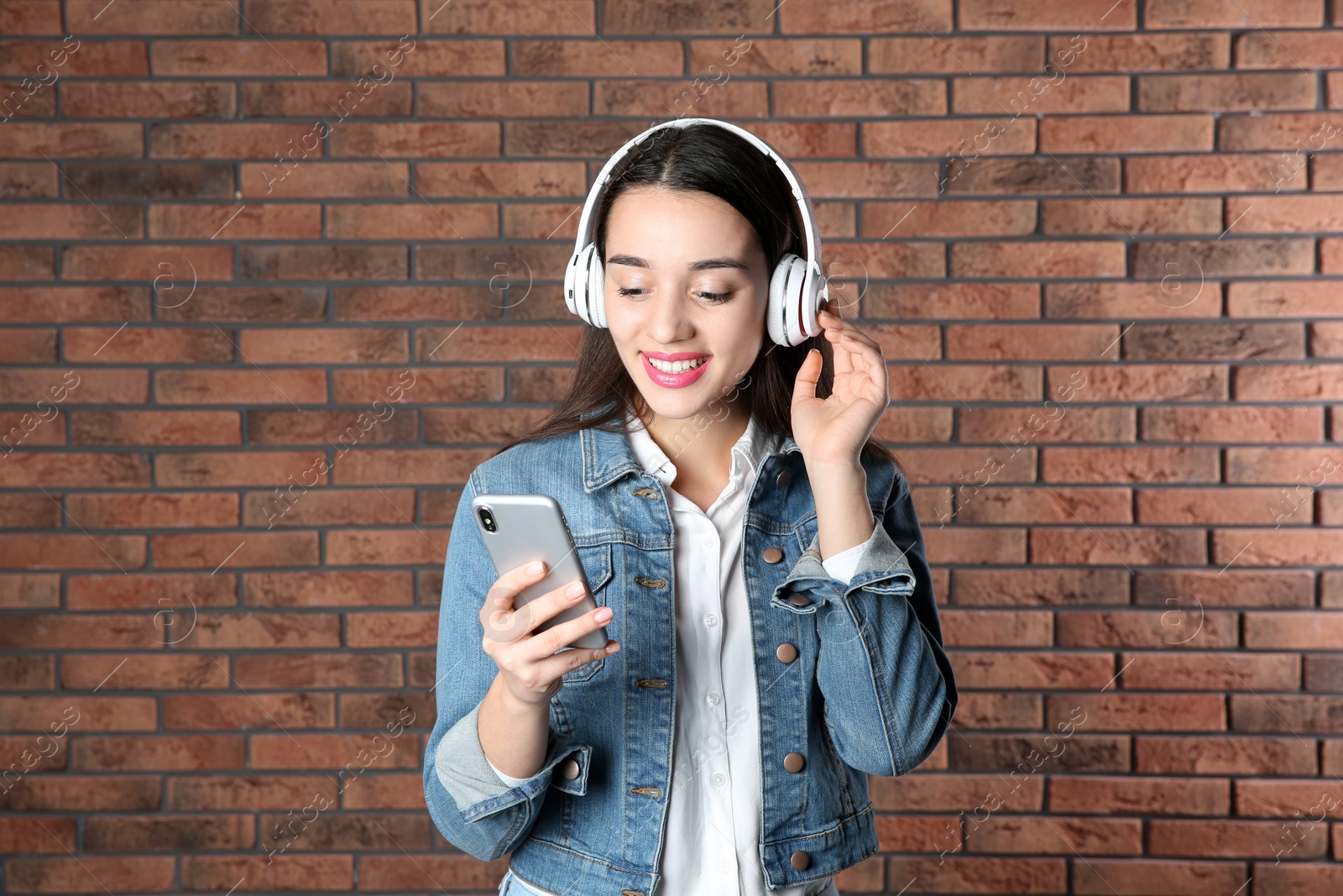 Photo of Beautiful young woman listening to music with headphones against brick wall