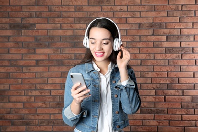 Photo of Beautiful young woman listening to music with headphones against brick wall