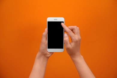 Photo of Young woman holding mobile phone with blank screen in hand on color background