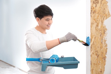 Male decorator painting wall with brush indoors