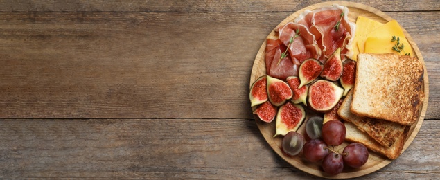 Photo of Delicious ripe figs, prosciutto and cheese served on wooden table, top view. Space for text