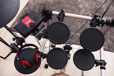 Photo of Modern electronic drum kit with headphones indoors, above view. Musical instrument