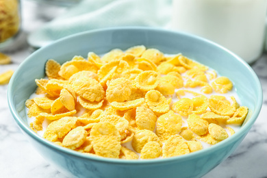 Tasty crispy corn flakes with milk on marble table, closeup