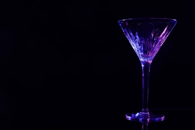 Beautiful martini glass on mirror table against black background. Space for text