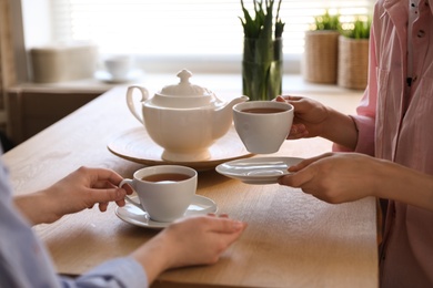 Photo of Women with cups of tea at table near window indoors, closeup