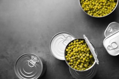 Tin cans and green peas on grey table, top view with space for text