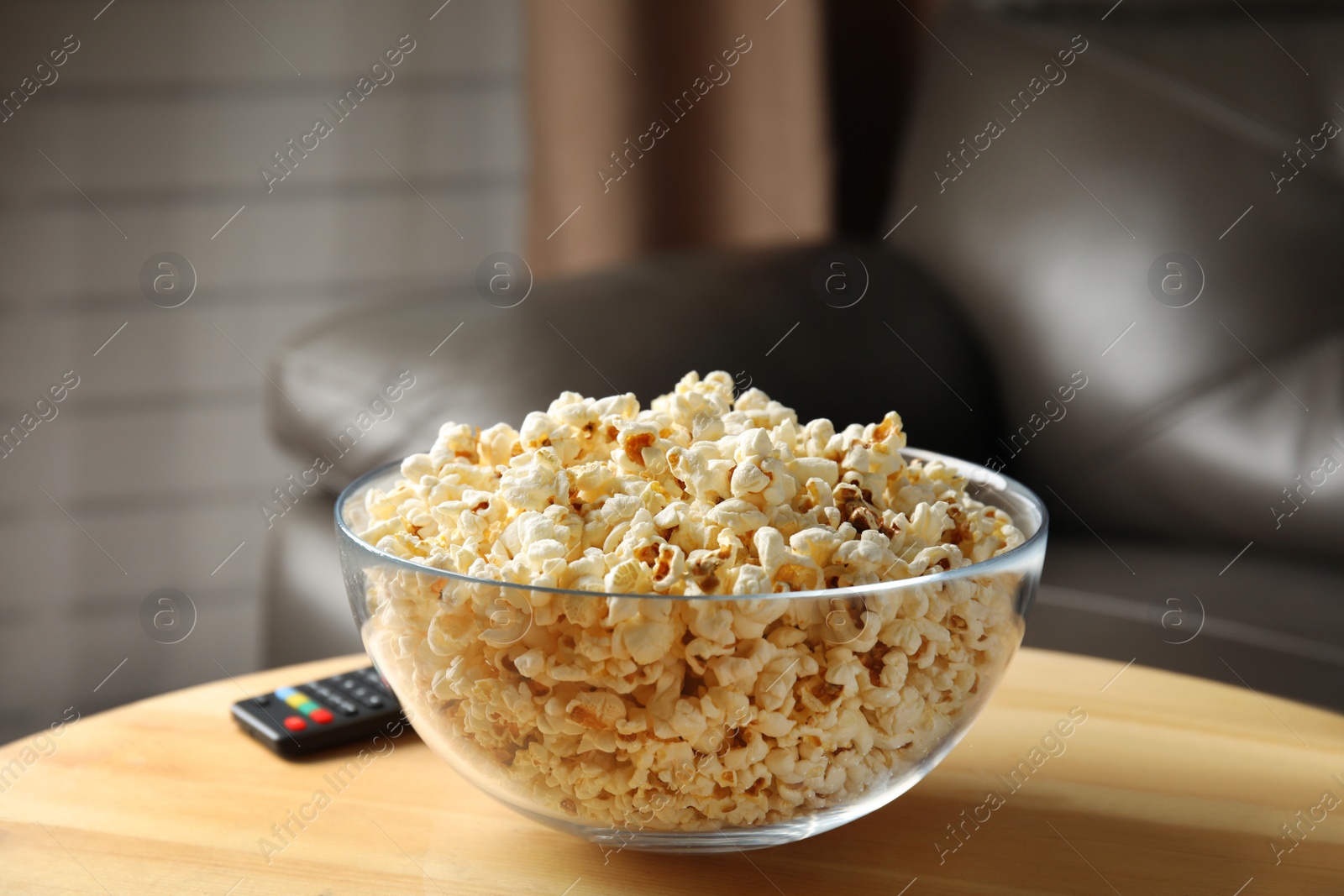 Photo of Bowl of popcorn and TV remote on table against blurred background. Watching cinema