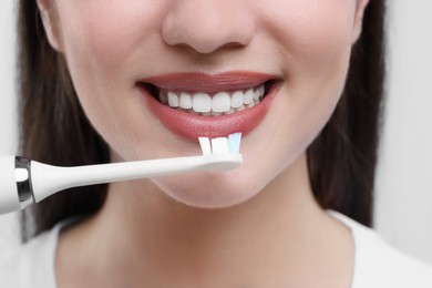 Woman brushing her teeth with electric toothbrush on white background, closeup