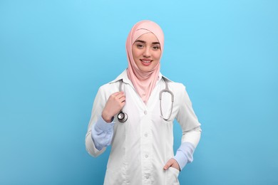 Muslim woman wearing hijab and medical uniform with stethoscope on light blue background