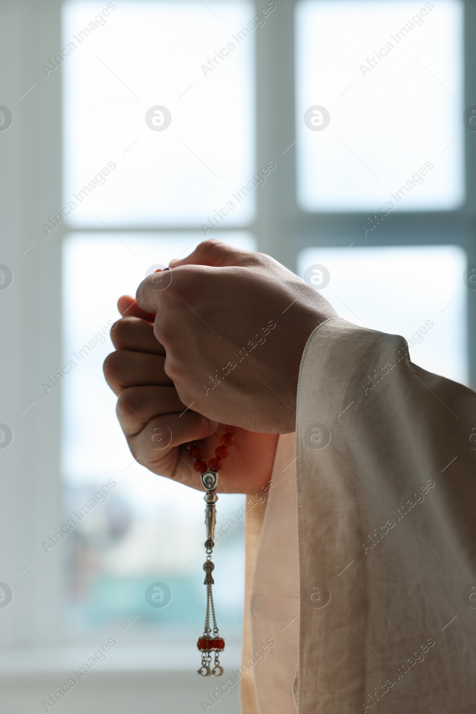 Photo of Muslim man with misbaha near window indoors, closeup