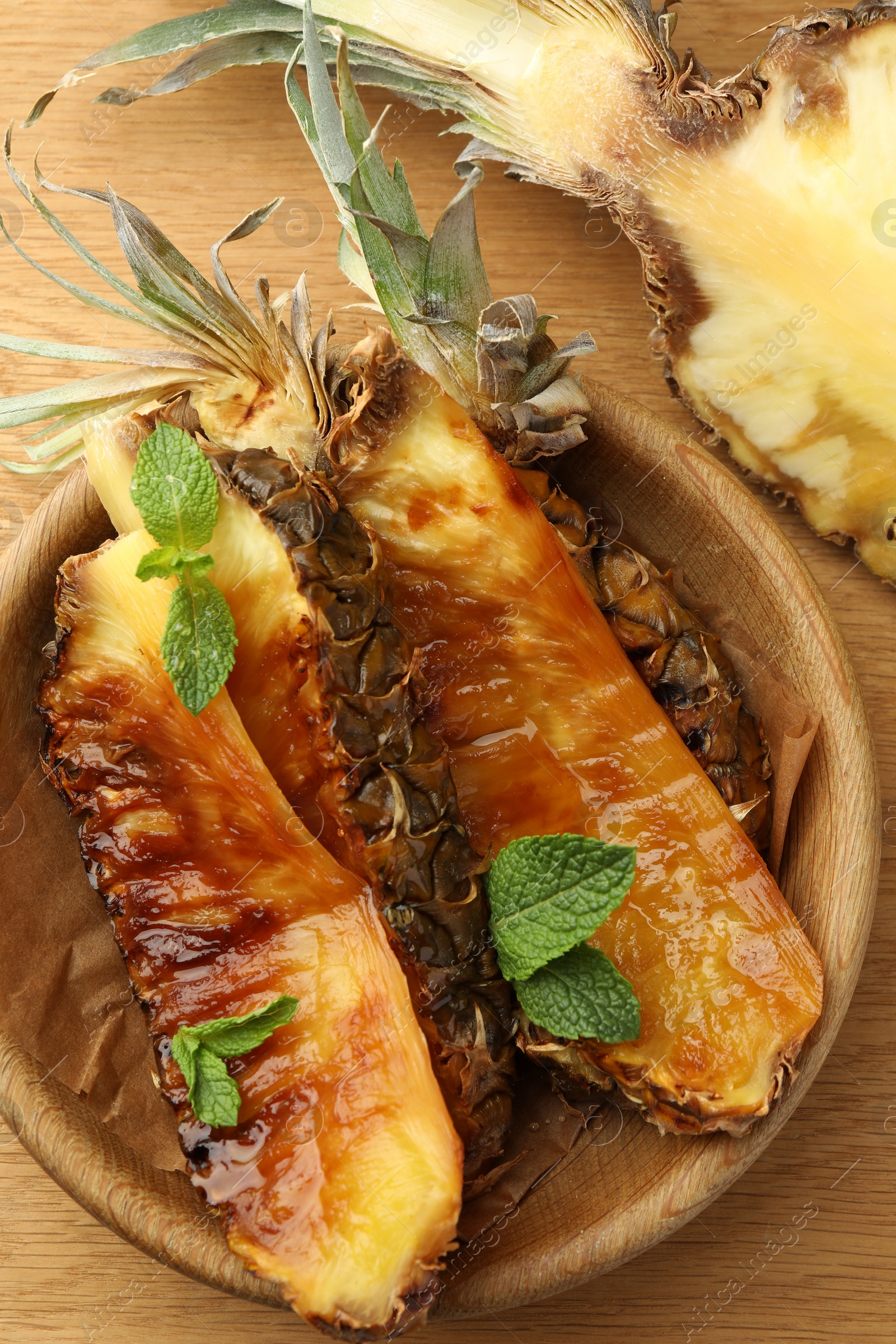 Photo of Tasty grilled pineapples in bowl on wooden table, top view