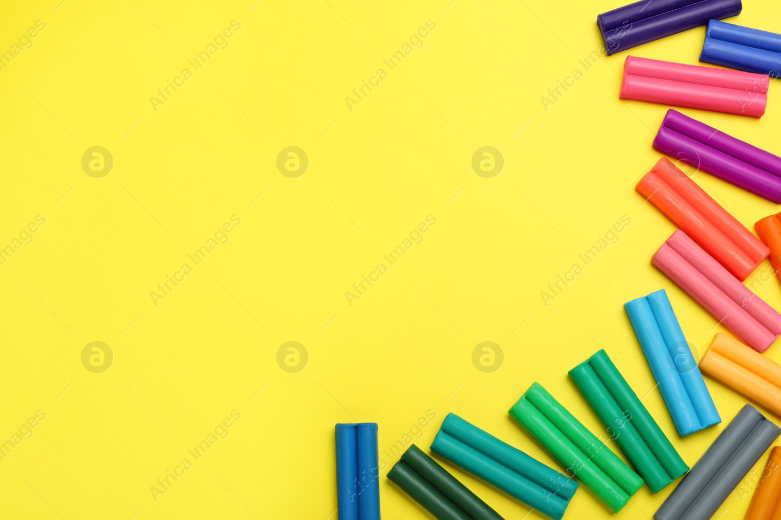 Photo of Colorful plasticine on yellow background, flat lay. Space for text