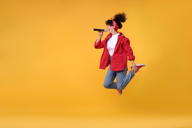 Photo of Beautiful young woman with microphone singing and jumping on yellow background. Space for text