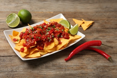 Photo of Plate of delicious mexican nachos chips with salsa sauce, lime and chili peppers on wooden table