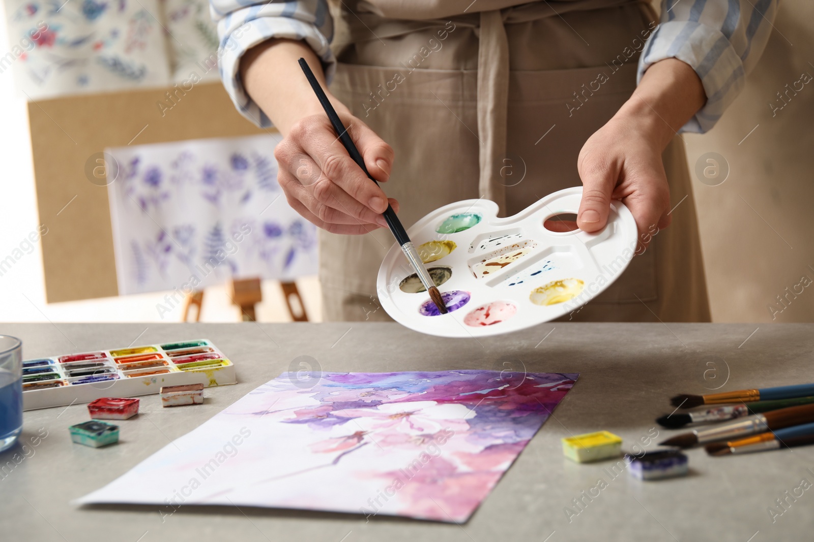 Photo of Woman painting flowers with watercolor at grey stone table in workshop, closeup