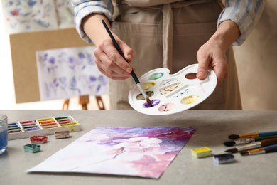 Woman painting flowers with watercolor at grey stone table in workshop, closeup