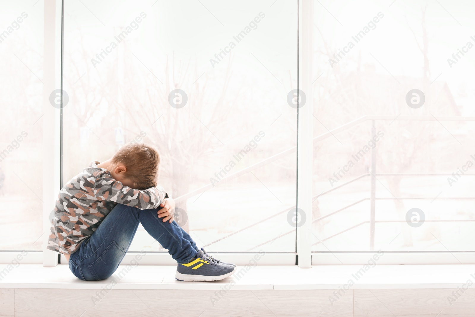 Photo of Lonely little boy near window indoors. Child autism