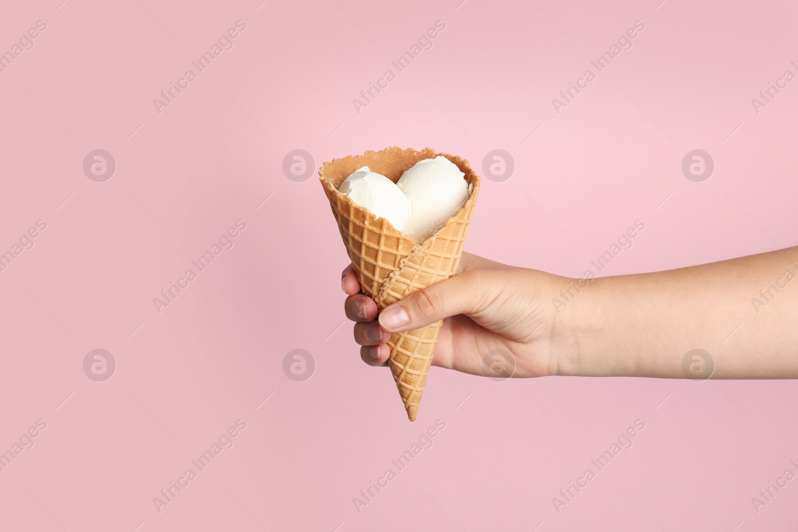 Photo of Woman holding delicious ice cream in wafer cone on pink background, closeup